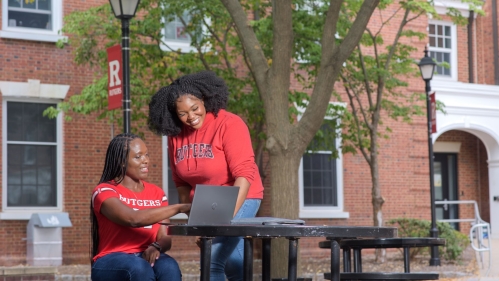 Students at a table outside on campus looking at a laptop