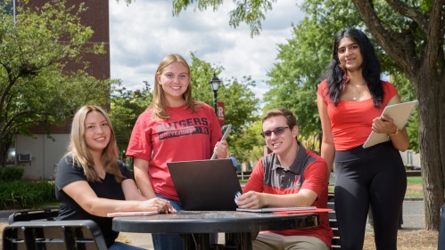 Students gathered around a table, smiling, outside on Rutgers campus