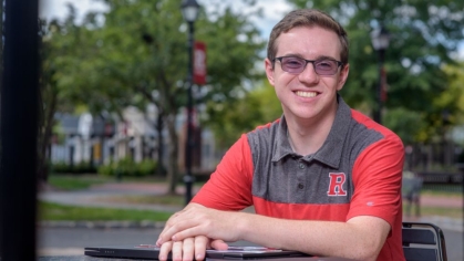 Student sitting and smiling at a table outside on the Rutgers campus